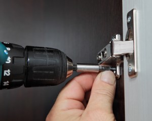 Carpenter tool when assembling furniture, close-up keyless chuck cordless screwdriver, screwing a screw door hinge.